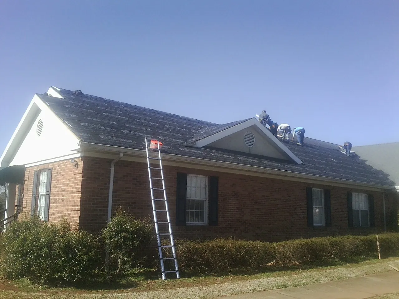 Crew tearing shingles off a brick ranch roof with a ladder set — Emergency Roof Repair work by our crew in Walpole