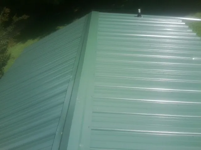 New green metal panels meeting at the ridge of a roof — Flat Roof Repair work by our crew in Walpole