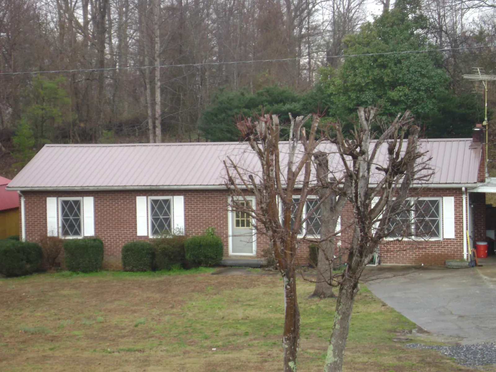 Mauve metal roof on a brick ranch home behind bare trees in Walpole